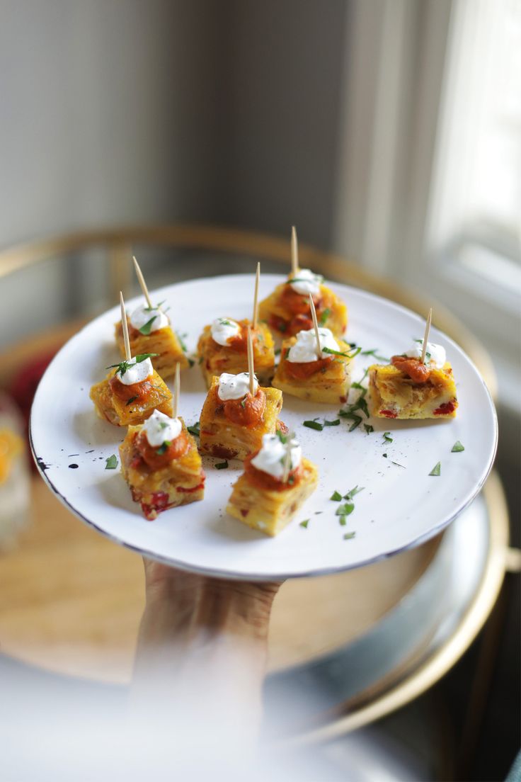 small appetizers with toothpicks are on a white plate in front of a window