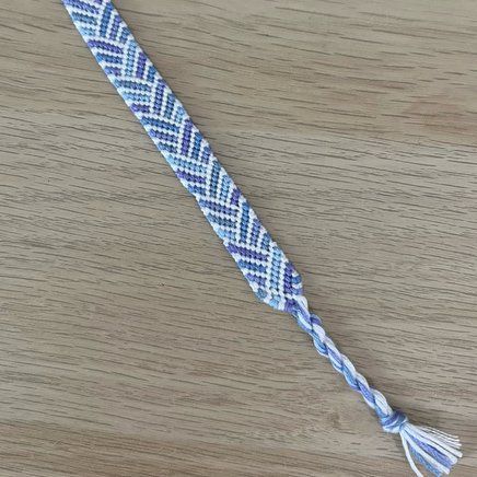 a blue and white braided bracelet with tassels on a wooden table top