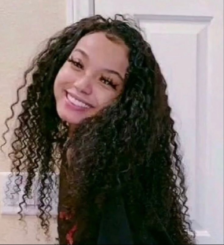 a woman with long curly hair standing in front of a door smiling at the camera