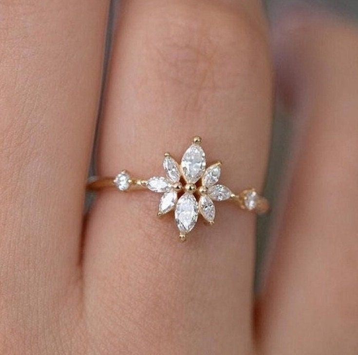 a woman's hand with a diamond ring on top of her finger and an open flower