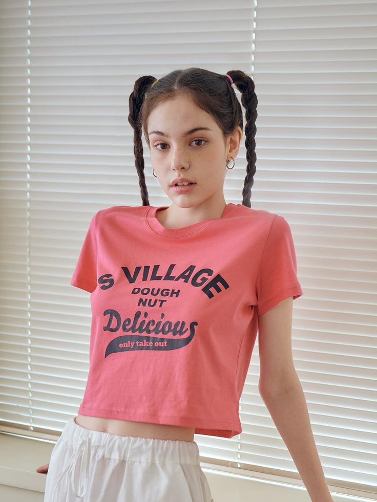 a girl with pigtails wearing a pink t - shirt that says village doughnut delicious