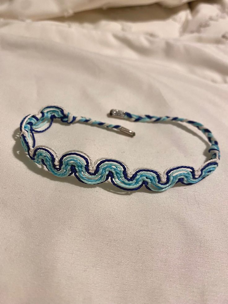 a blue and white braided bracelet sitting on top of a white bed covered in sheets