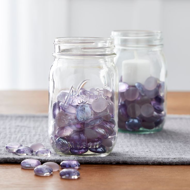 two glass jars filled with purple beads on top of a table