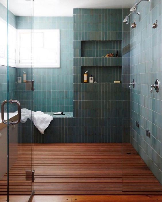 a green tiled bathroom with wood flooring and glass shower door, built in shelves on the wall