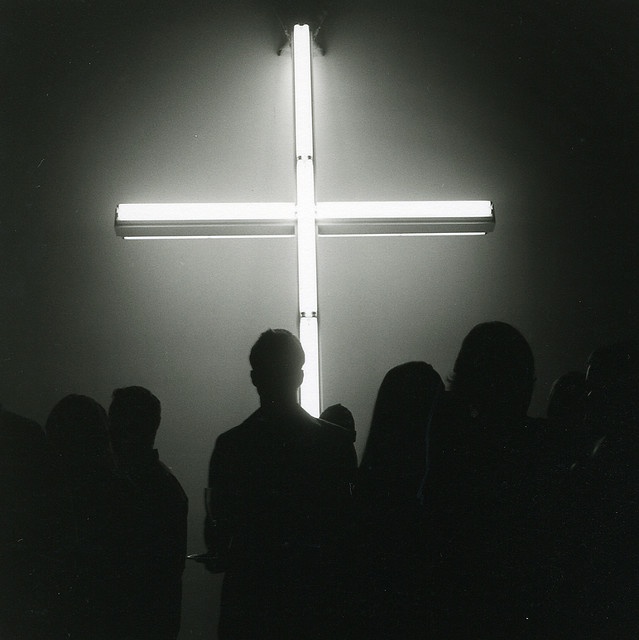 people standing in front of a cross with the light shining on it's side