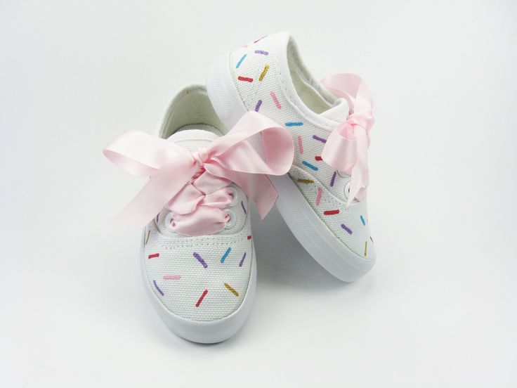 pair of white shoes with pink bow and sprinkles on the soles