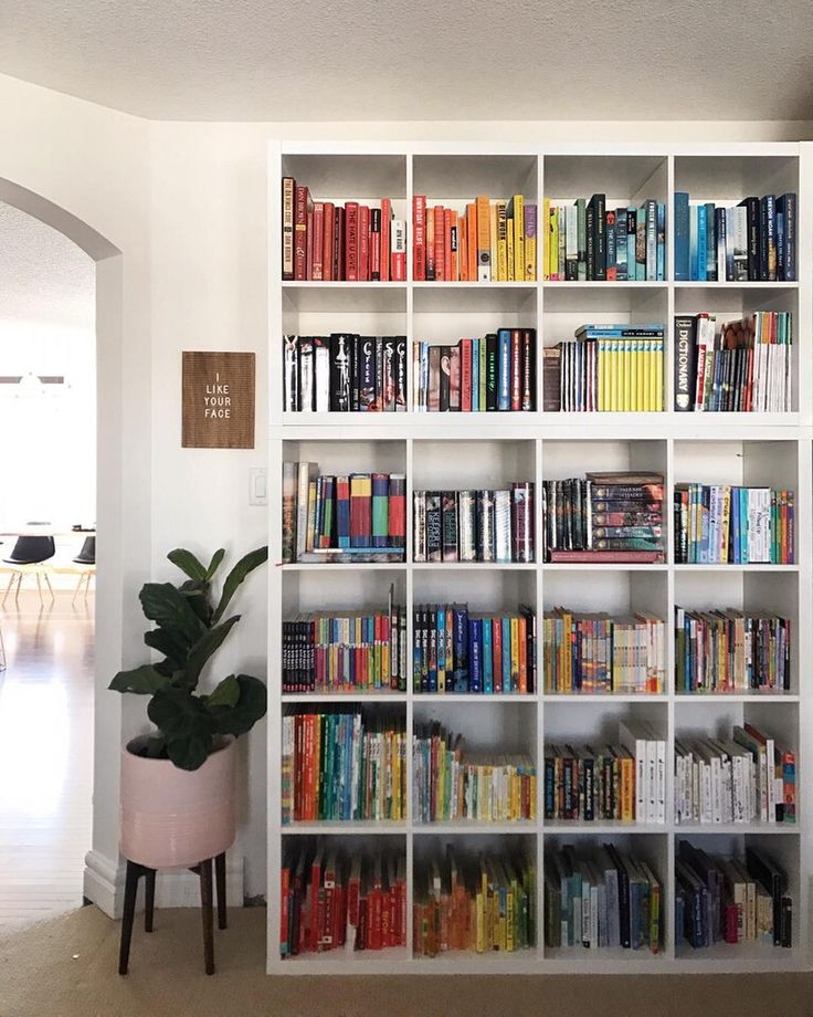 a white bookcase filled with lots of books next to a plant in a living room