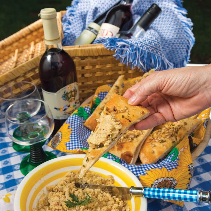 a person holding a piece of bread over a bowl of food on a picnic table