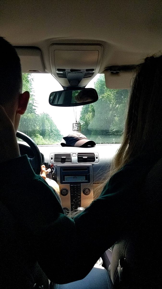 two people driving in the back seat of a car with their hands on the steering wheel