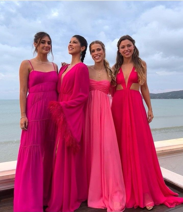 three women in pink dresses standing next to each other near the ocean with their arms around one another