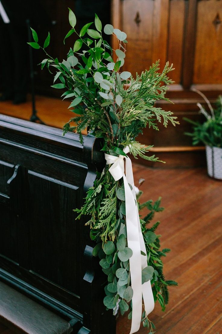 a bunch of greenery tied to the back of a church pew with a white ribbon