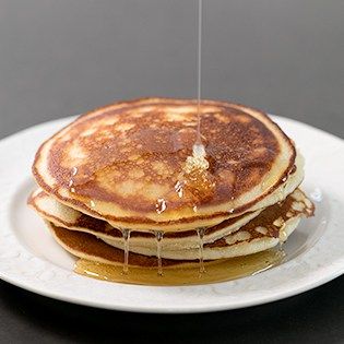 a stack of pancakes sitting on top of a white plate with syrup pouring over them