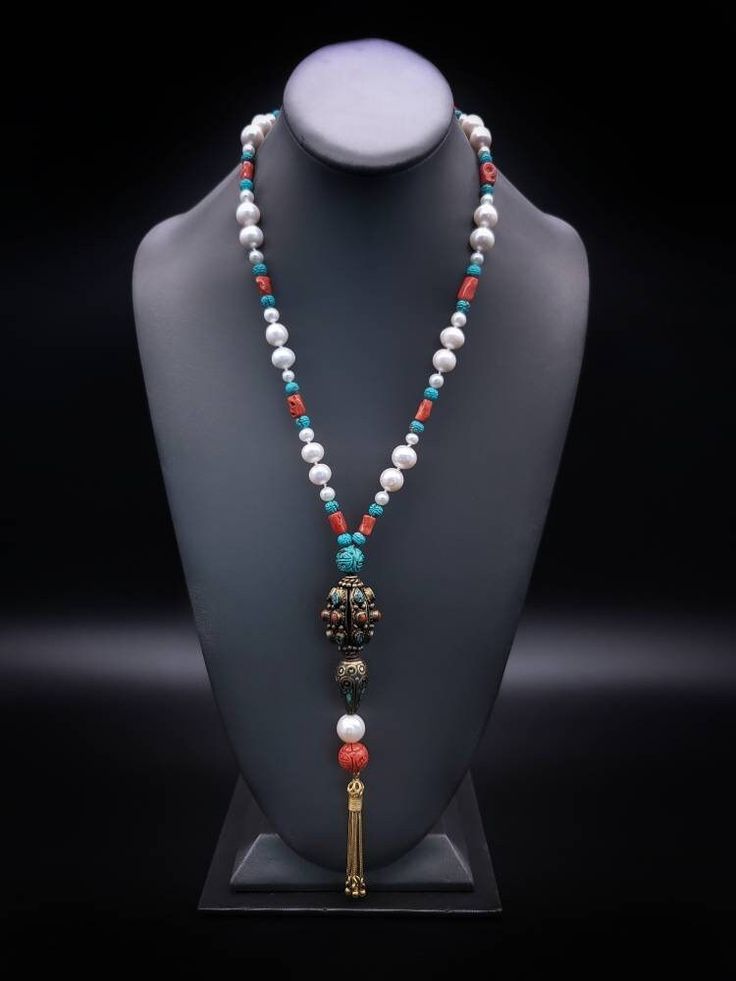 "Description and Details  Discover the beautiful Tibetan jewelry masterpiece that represents a blend of traditional and modern elements in this One-of-a-kind Deluxe long necklace!  Freshwater Pearls, Coral, and Turquoise are designed to enhance the beauty of the handmade Tibetan pendant featured in the necklace.  One-of-a-kind  Item: E 450 Freshwater Pearl  Turquoise  Tibetan Silver, Turquoise  Carved Copal Tassel: Vermeil  Clasp: Vermeil  Approx. 29\" Silk hand-knotted" Elegant 108 Beads Jewelry Gift, Elegant Turquoise Beaded Lariat Necklace, White Spiritual Lariat Necklace, Spiritual White Lariat Necklace, Elegant Turquoise Long Necklace For Gift, Traditional Long Necklace With 108 Beads, Elegant Necklace With 108 Beads Pendant, Elegant Gemstone Beads For Meditation Jewelry, Elegant Gemstone Beads Jewelry For Meditation