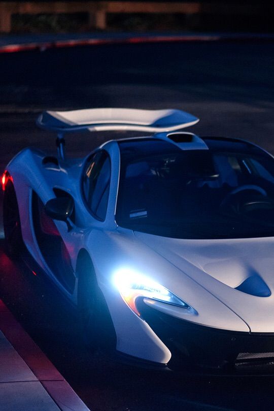 a white and blue sports car parked on the side of the road at night with its lights on