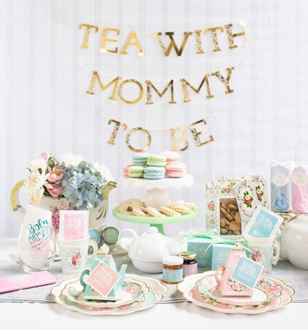 a table topped with plates and cups filled with food next to a sign that says tea with mommy to be