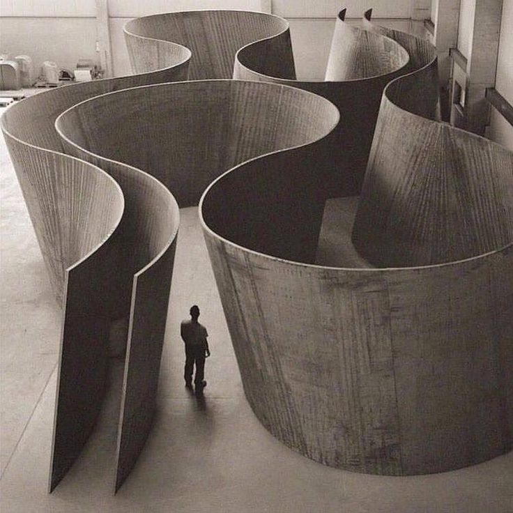 a black and white photo of a person standing in front of an abstract structure with curved sections