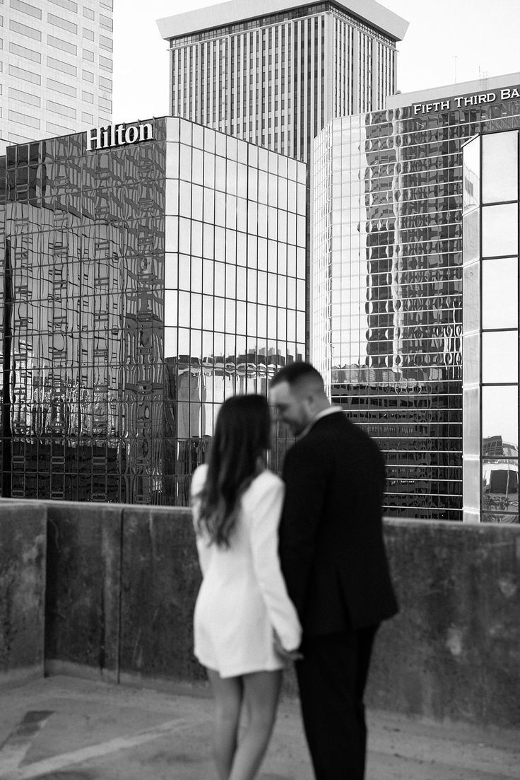 a man and woman standing next to each other in front of tall buildings with glass windows