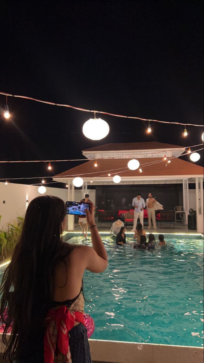 a woman taking a photo of people in the pool at night with their cell phones