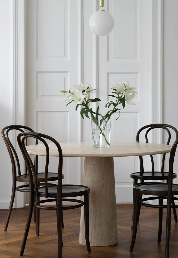 a table with four chairs around it and flowers in a vase on the table top