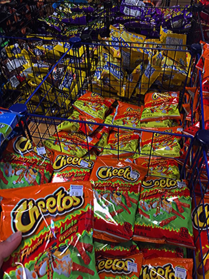 many bags of chips are stacked up in a grocery store and someone is holding one bag