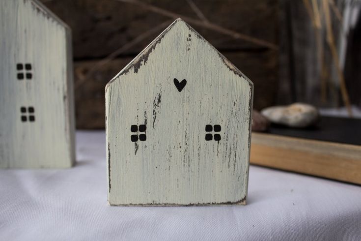 two small wooden houses sitting on top of a white cloth covered table next to a book