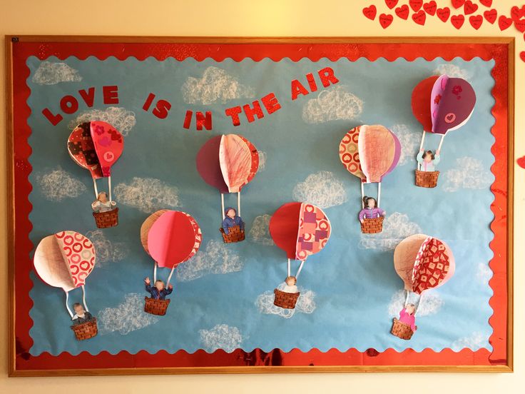 a bulletin board with hot air balloons on it and hearts hanging from the wall above