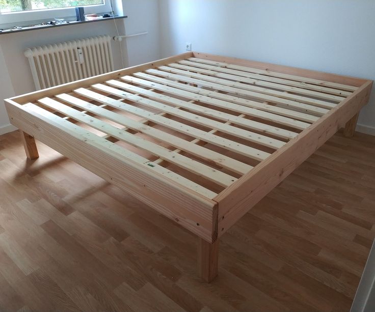 a wooden bed frame sitting on top of a hard wood floor next to a radiator