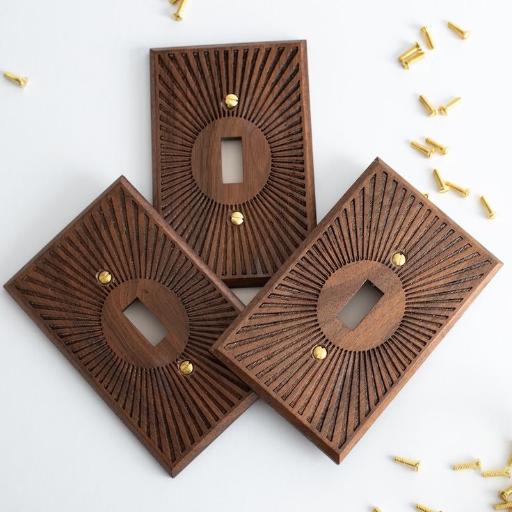 three decorative wooden pieces with holes in the middle and gold studs around them on a white surface