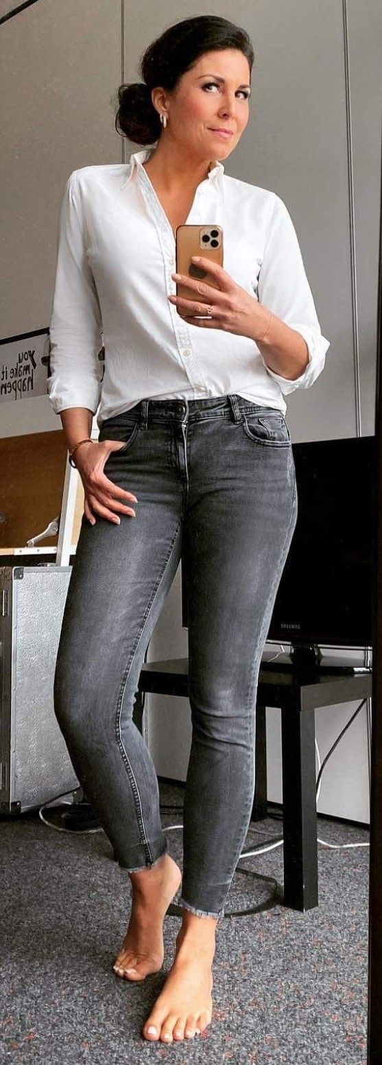 a woman in white shirt and jeans holding a cell phone