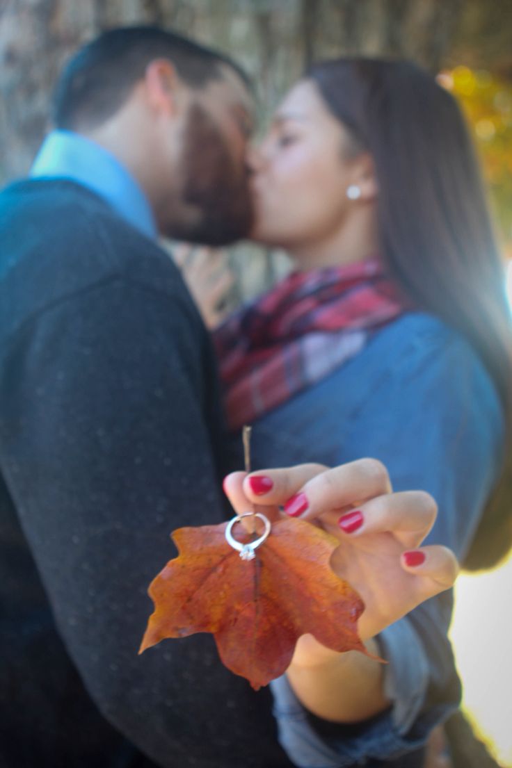 a man and woman kissing while holding an orange leaf