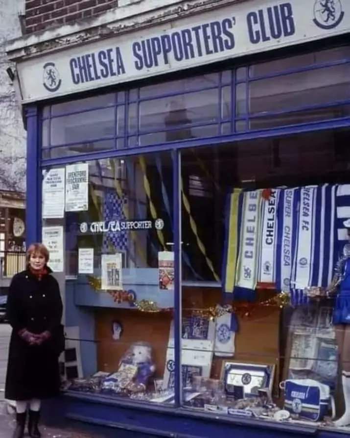 a woman standing in front of a store window with lots of items on display outside