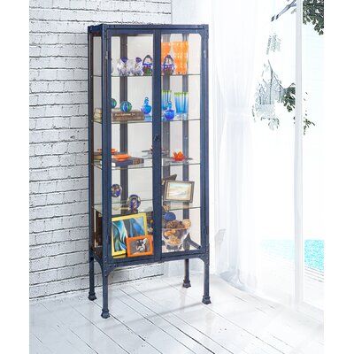 a tall glass display case with pictures on the front and bottom shelves, against a white brick wall