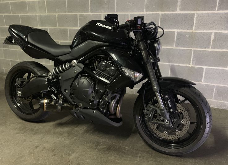 a black motorcycle is parked in front of a brick wall and cement flooring area