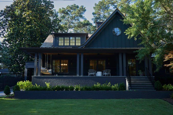 a house that is sitting in the grass next to some trees and bushes with a clock on it's face