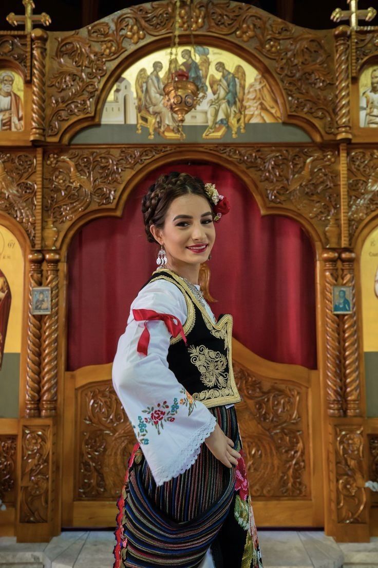 a woman is standing in front of an ornate wooden alter with red curtains behind her