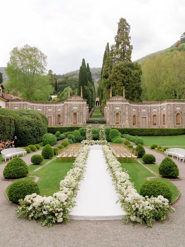 an outdoor ceremony setup with white flowers and greenery in the center, surrounded by hedges