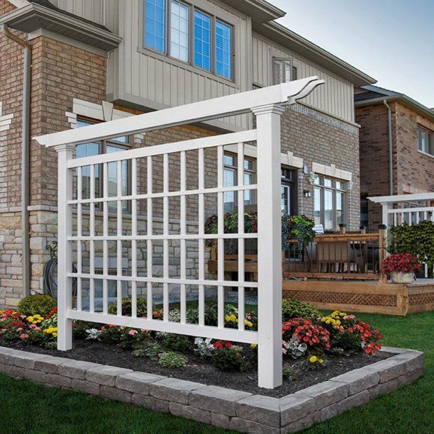 a white trellis sitting in front of a brick building next to a flower bed