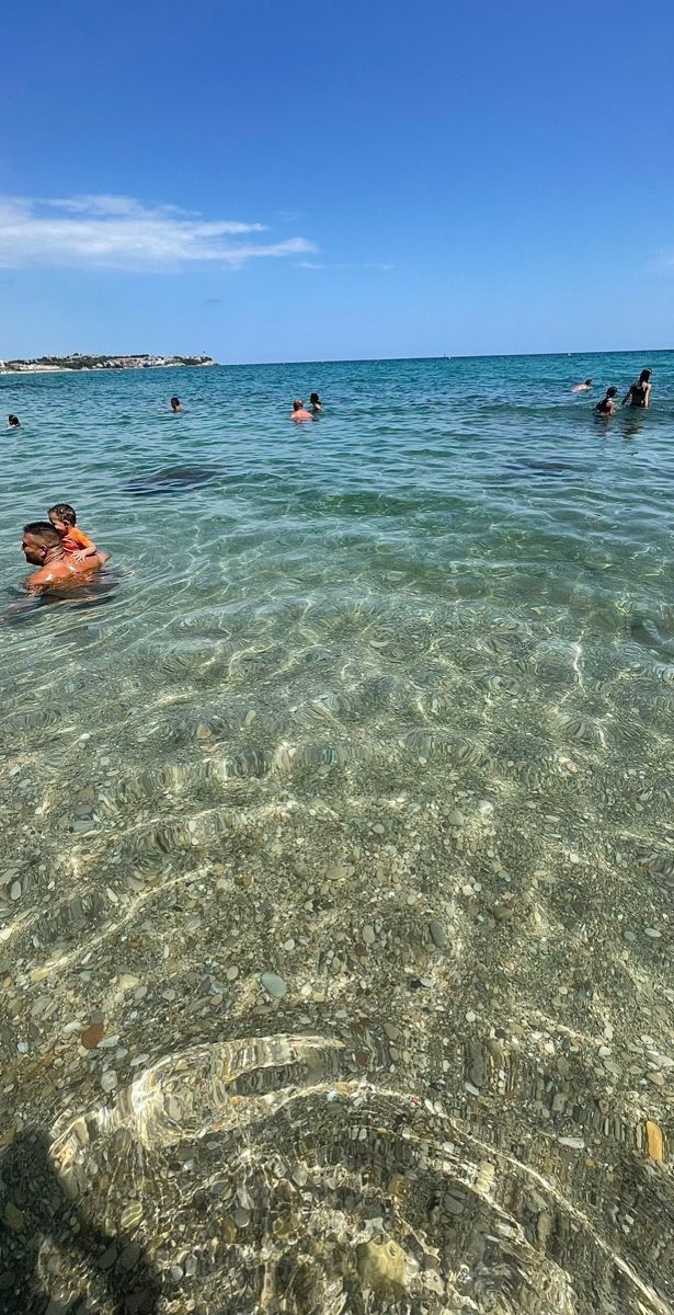 people swimming in the ocean on a sunny day with clear blue skies and shallow water