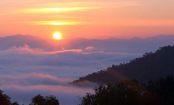 the sun is setting over some mountains covered in fog and low lying clouds with trees below