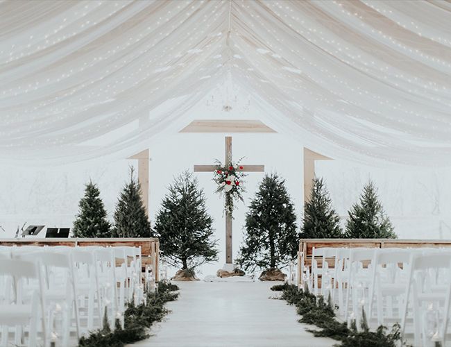 an outdoor wedding setup with white chairs and greenery on the aisle, decorated with christmas trees