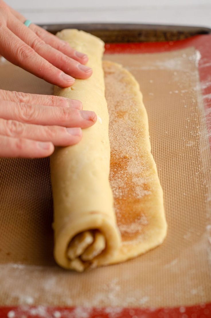 a person reaching for a pastry roll on a baking sheet in the process of being rolled up