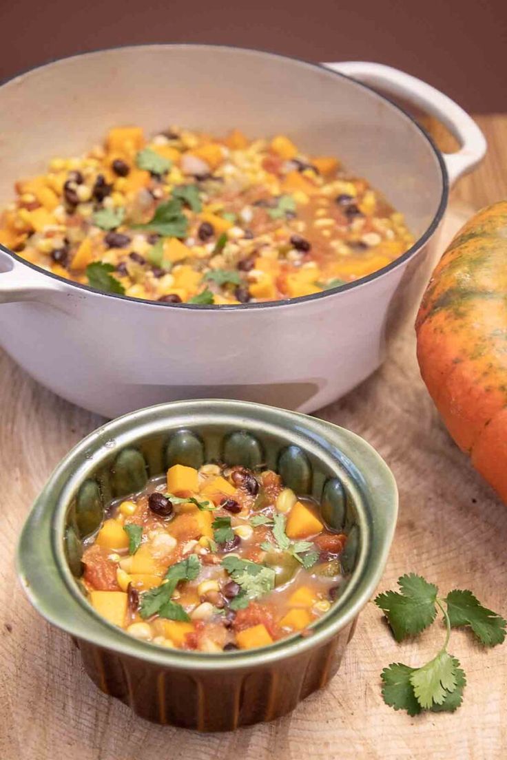 two bowls filled with food sitting on top of a wooden table next to an orange pumpkin