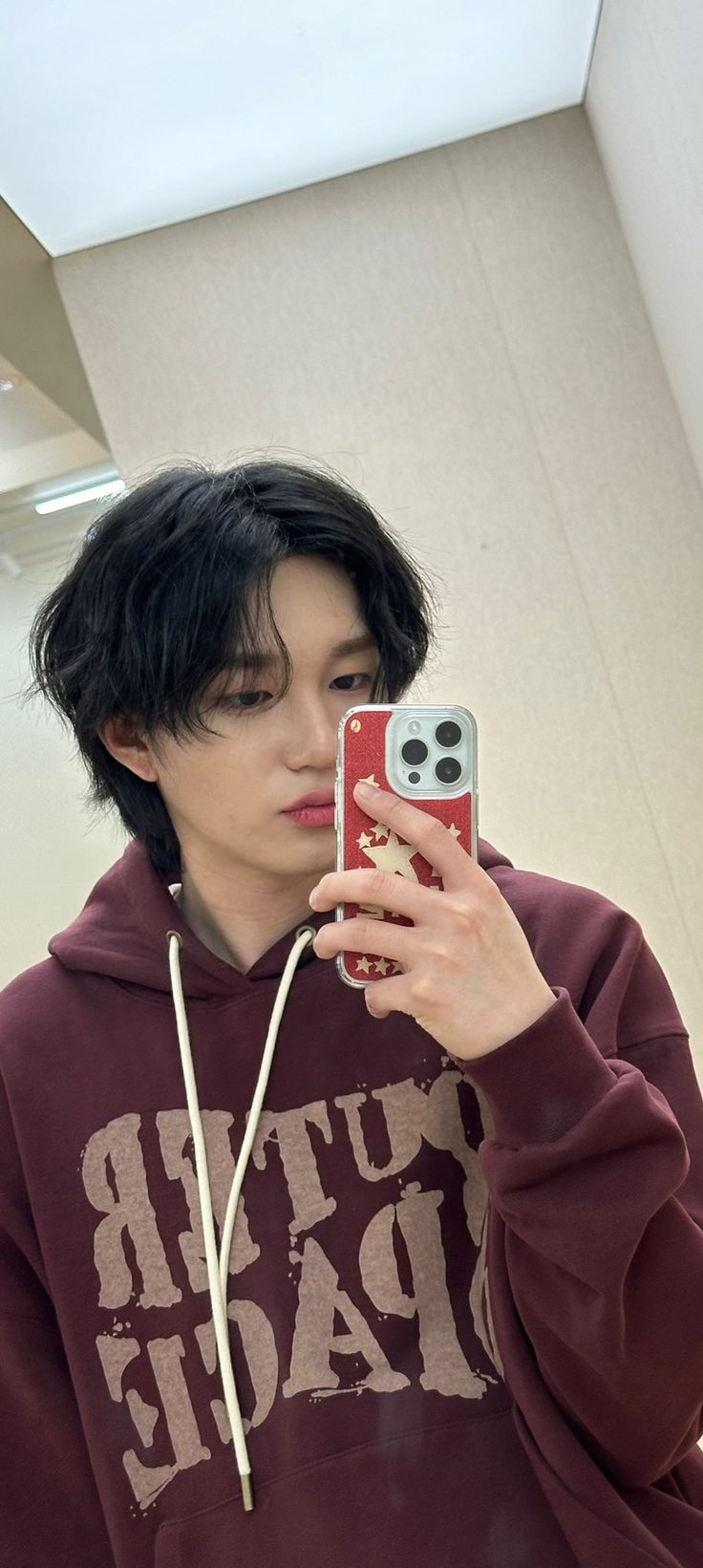 a young man taking a selfie with his cell phone in front of him and wearing a maroon hoodie