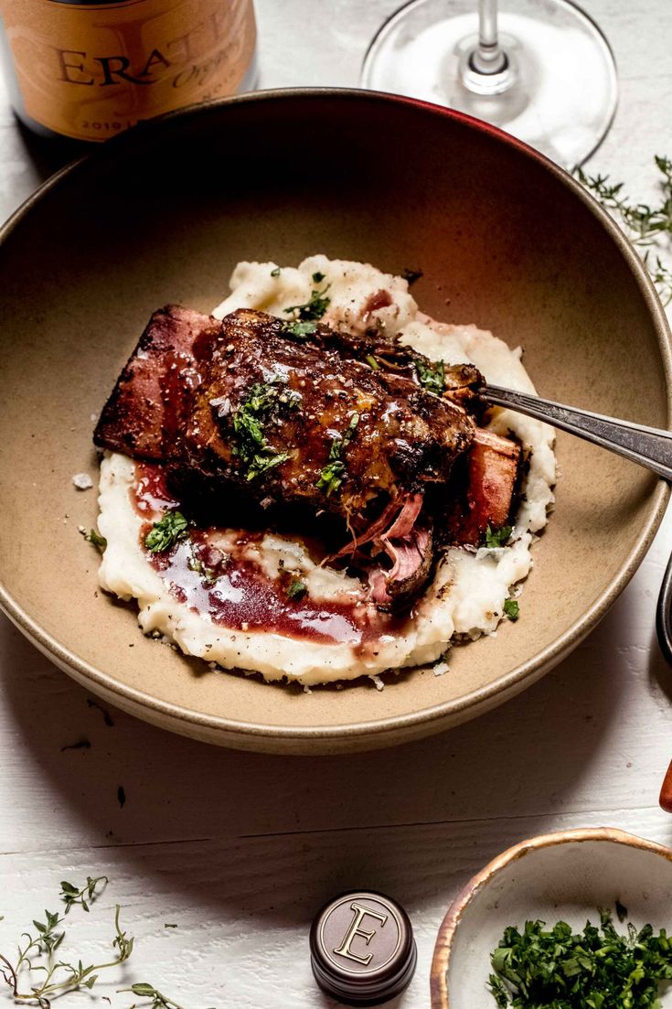 a plate with meat and mashed potatoes on it next to a bottle of wine