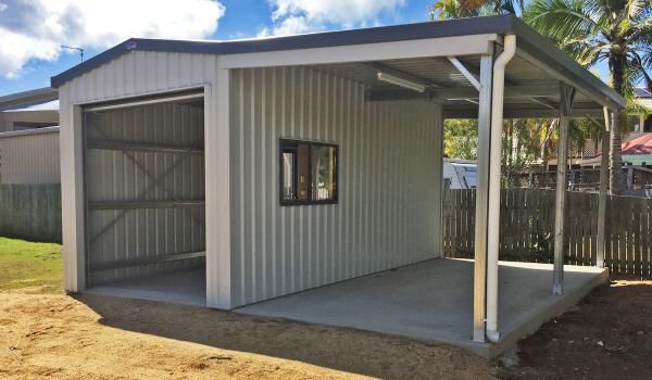 a white shed sitting on top of a dirt field next to a fence and palm trees