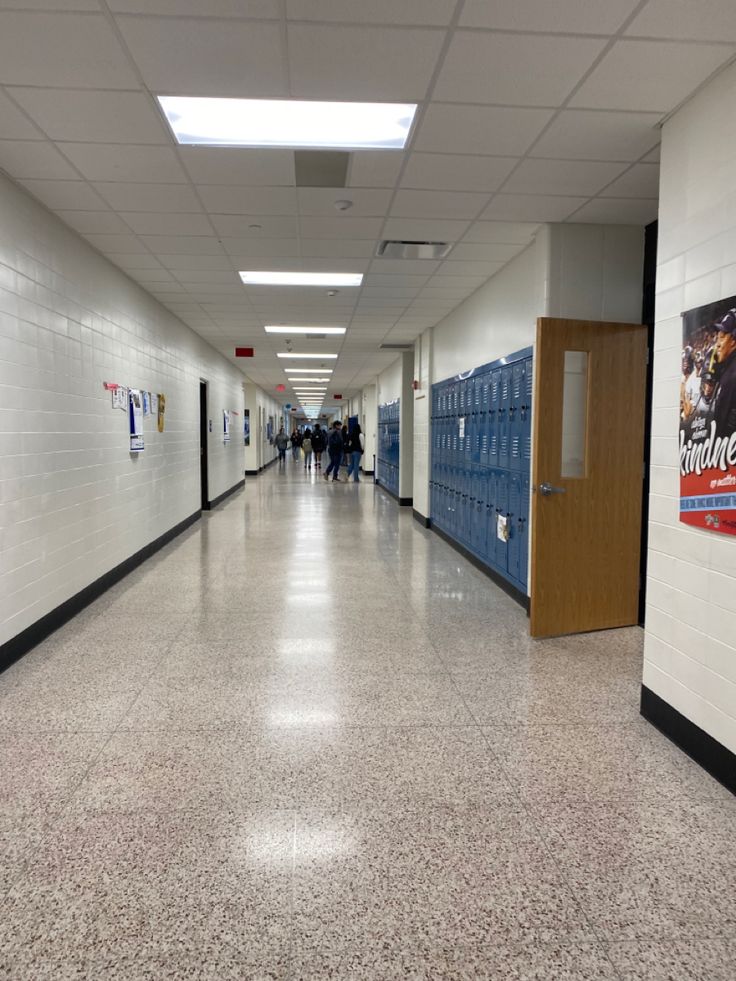 an empty hallway with blue lockers and people walking down the corridor on either side