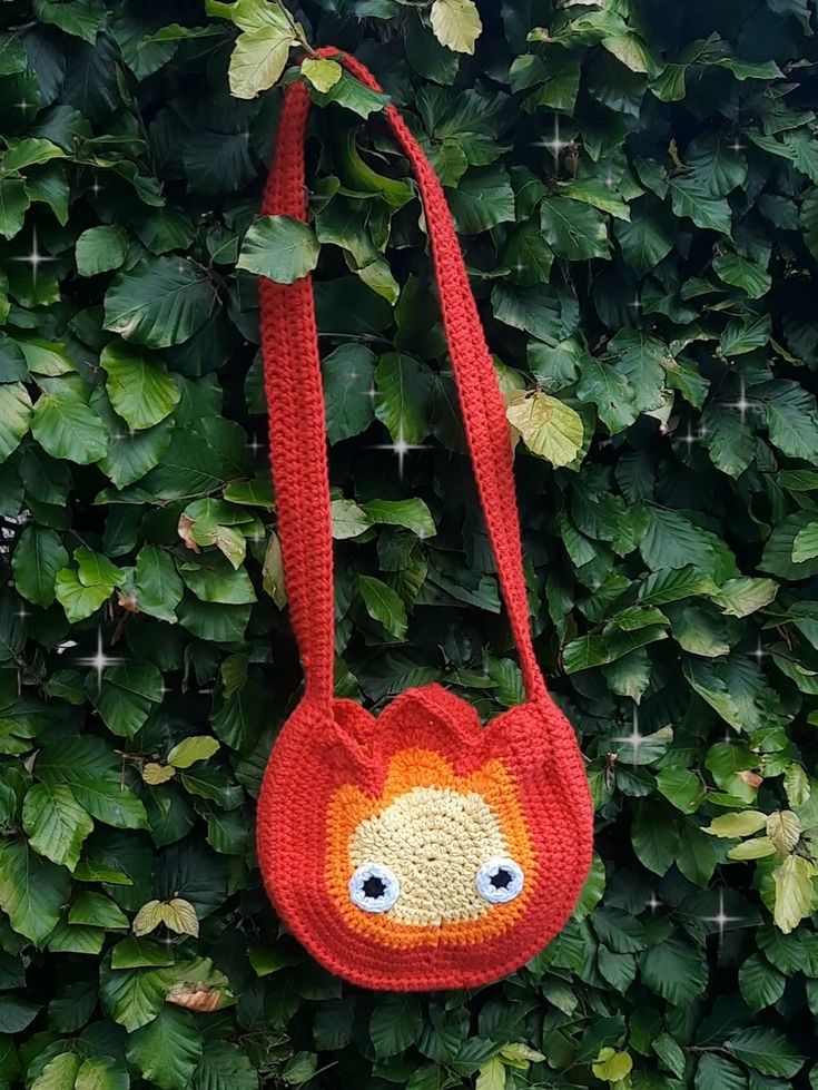 a crocheted bag hanging from a tree with leaves around it and eyes drawn on the front