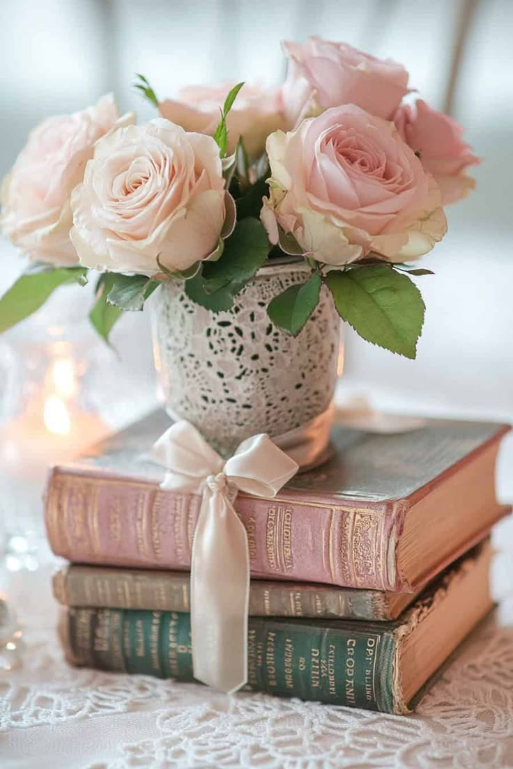 three books stacked on top of each other with pink roses in the middle and candles behind them