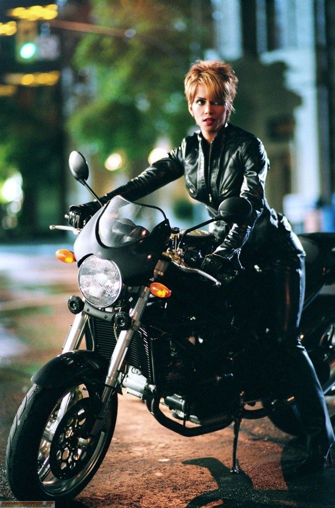 a woman sitting on top of a black motorcycle in the street at night with her hand on the handlebars