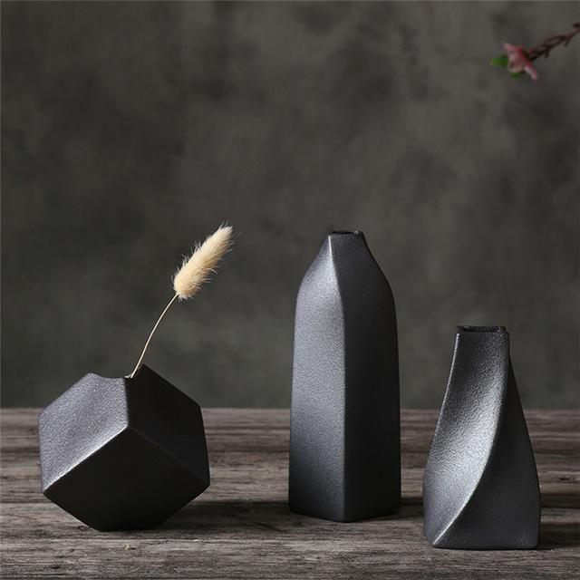 three black vases sitting on top of a wooden table next to a flower in a vase